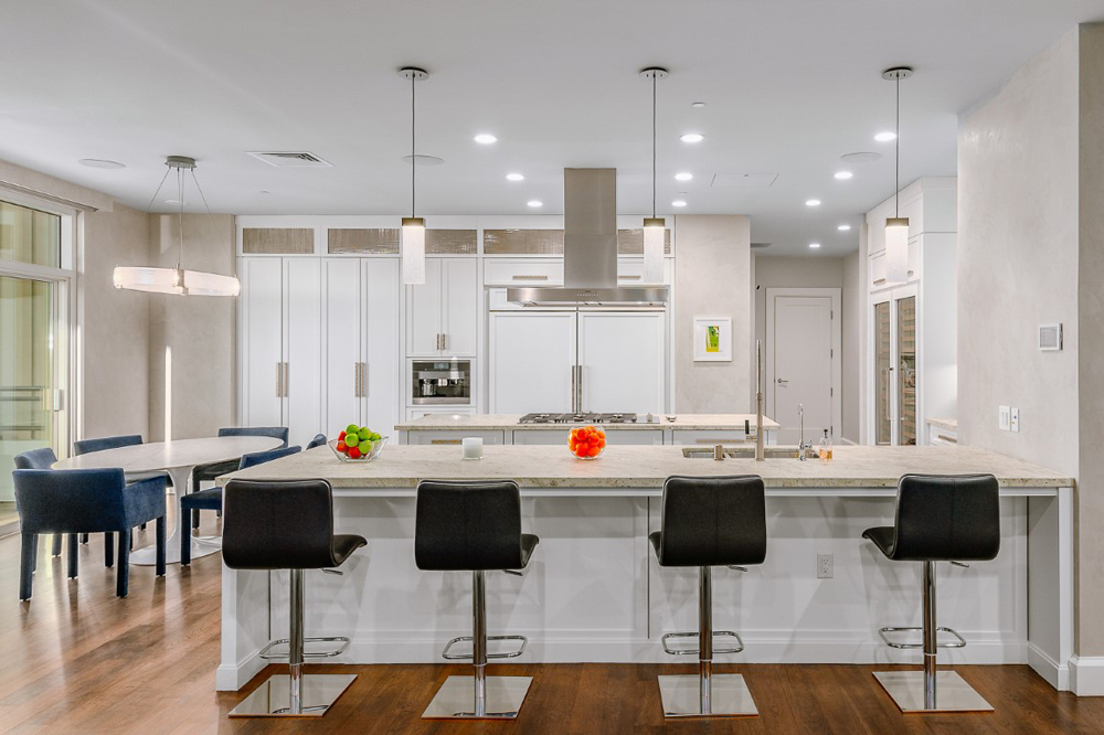 A large white kitchen with a spacious island with seating for four and a smaller dining area off to the left-hand side