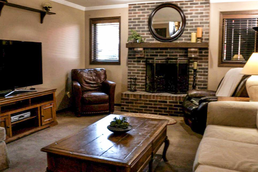 A dark and dated basement den with a heavy brick fireplace