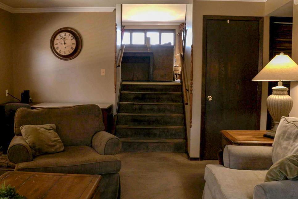 A bland, brown basement den with carpeting and outdated furniture