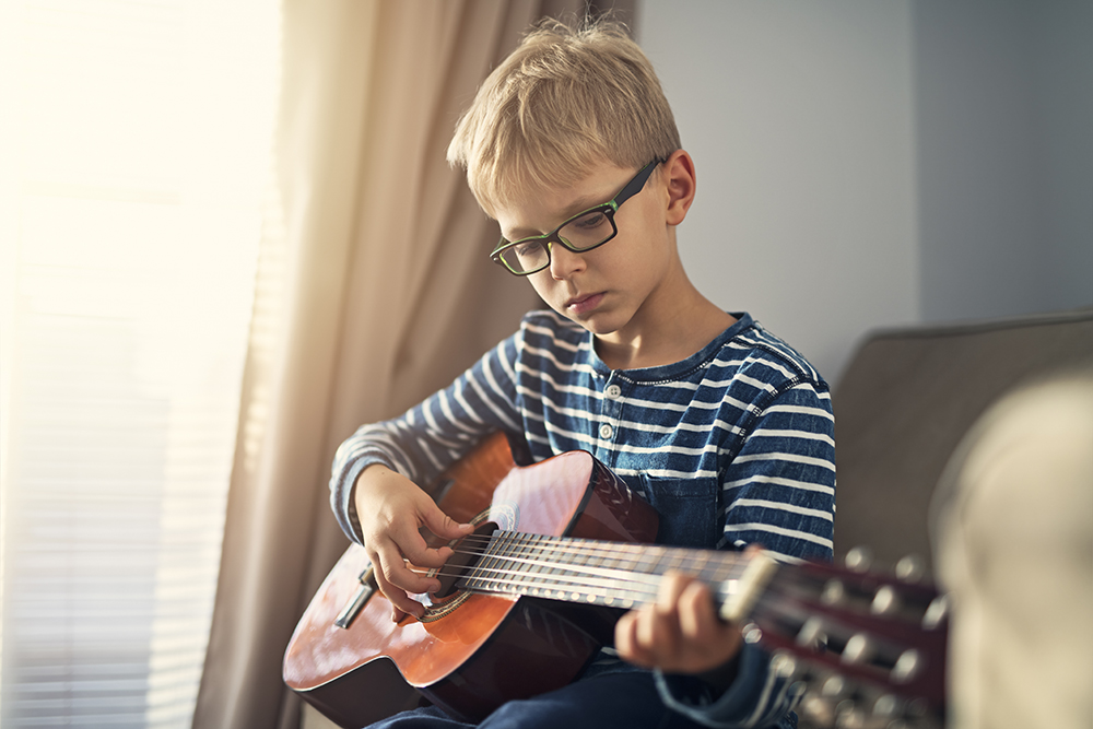 Little boy with glasses playing a guitar