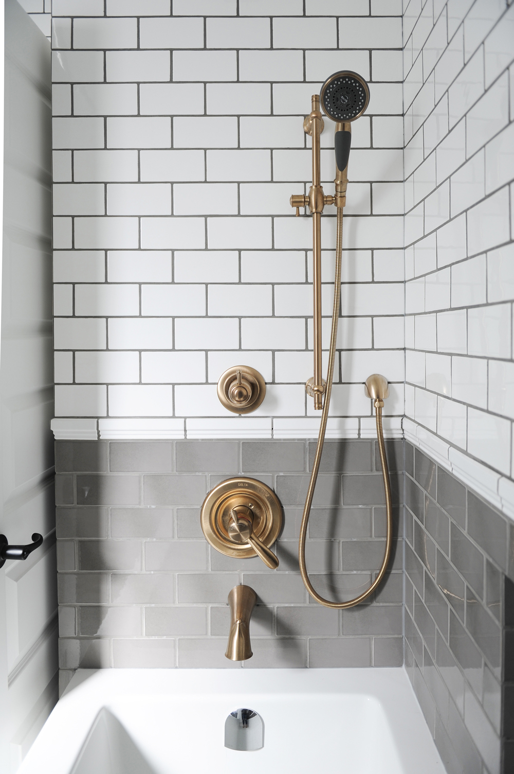 Brass exposed pipes in a renovated shower with grey and white tiles