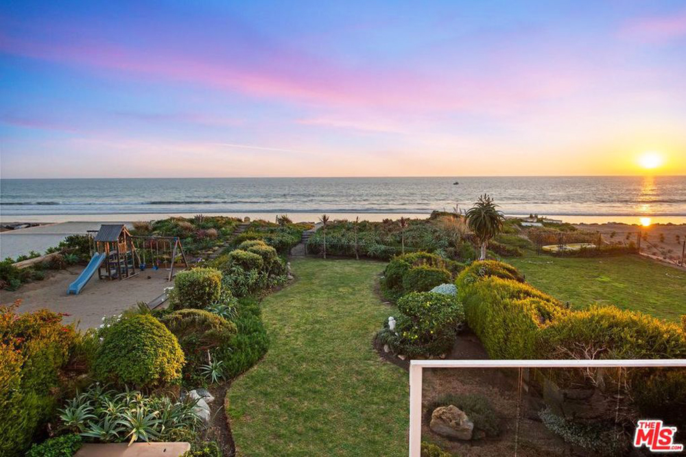 An expansive backyard with landscaped shrubs and trees, separate child's playground and views of the nearby beach
