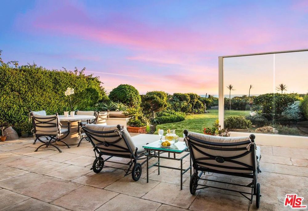 The backyard patio area with reclining chairs overlooking a landscaped yard and nearby beach