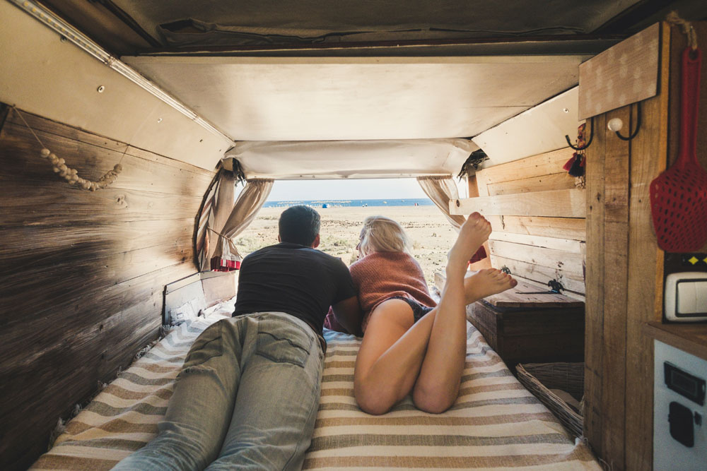 A young couple looking out the back open door of their rustic mobile home