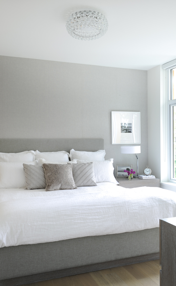 Grey bed with white bedding and one side table visible