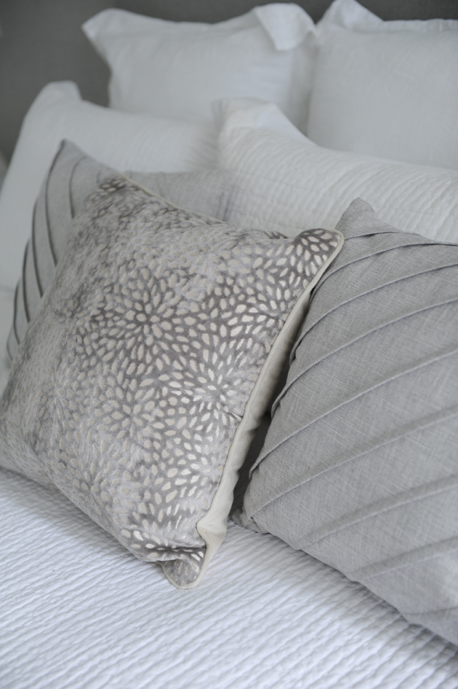 Close up of two grey textured cushions on bed, one petal patterned in middle