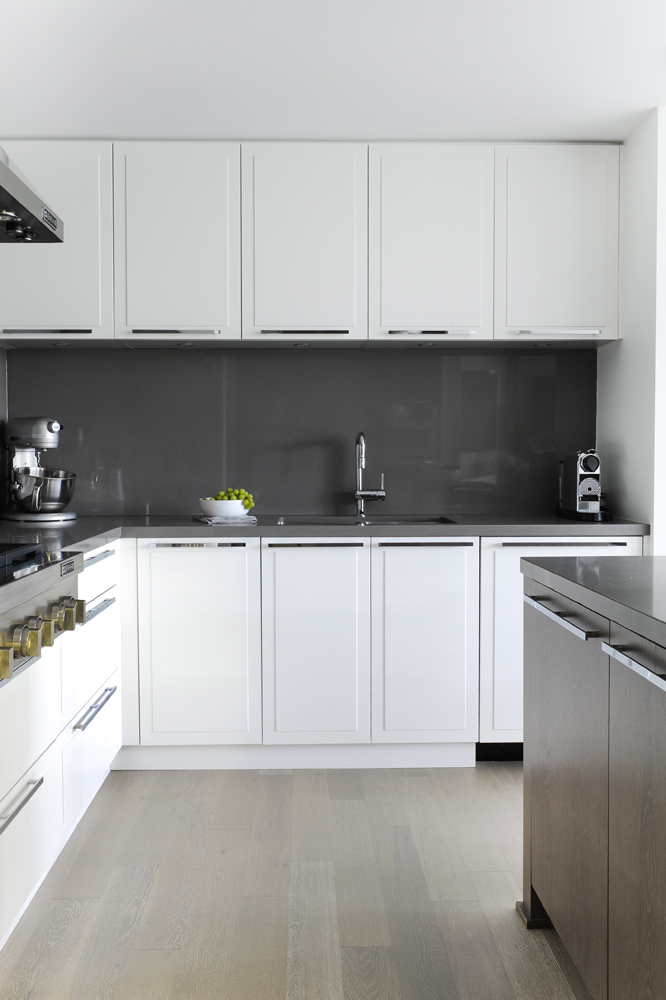 Grey glass kitchen backdrop with upper and lower white cupboards, grapes in bowl