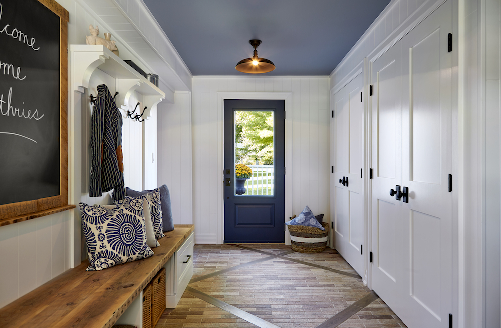A modern mudroom off the main entrance with a wooden bench, chalkboard and patterned throw pillows