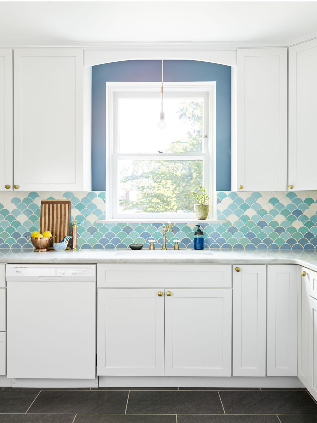 A blue fish-scale backsplash with white kitchen cabinets