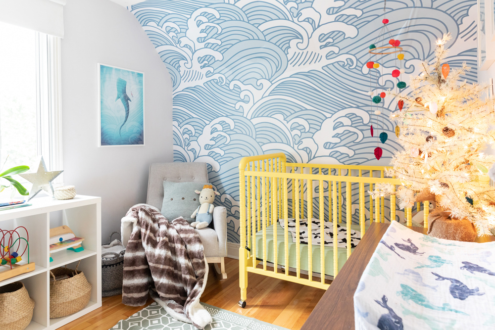 A whimsical, ocean-inspired nursery with blue and white wallpaper and whale-print art and blankets