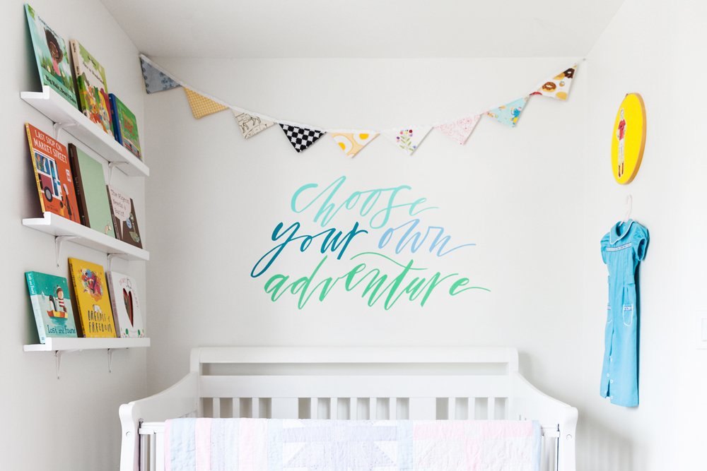 An all-white nursery with random pops of colour on the bookshelf and hanging from the wall