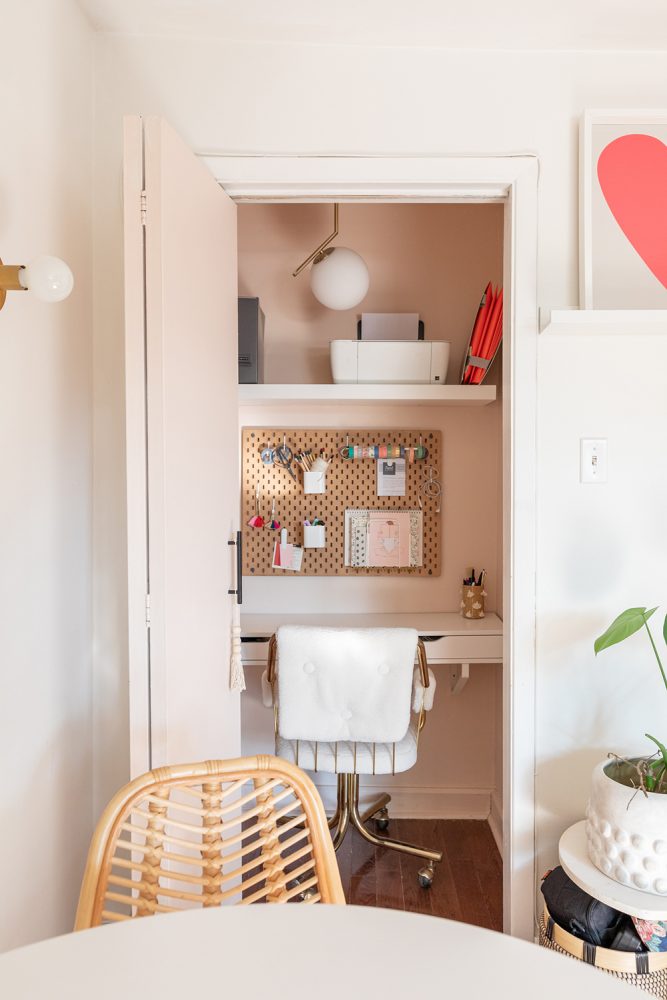 A tiny narrow closet painted pink and transformed into a small office space with a desk and corkboard organizer