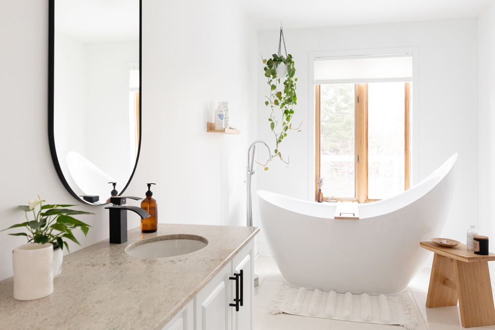 A pristine white bathroom, brightly lit, with a large soaker tub in the centre by the window