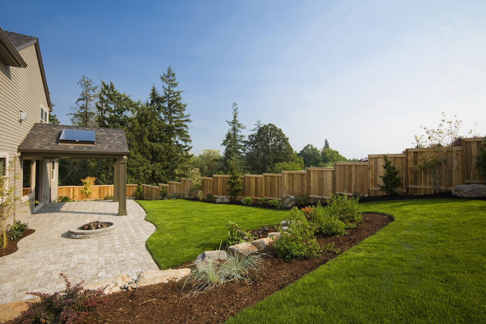 A perfectly landscaped, fenced backyard with bushes and small trees