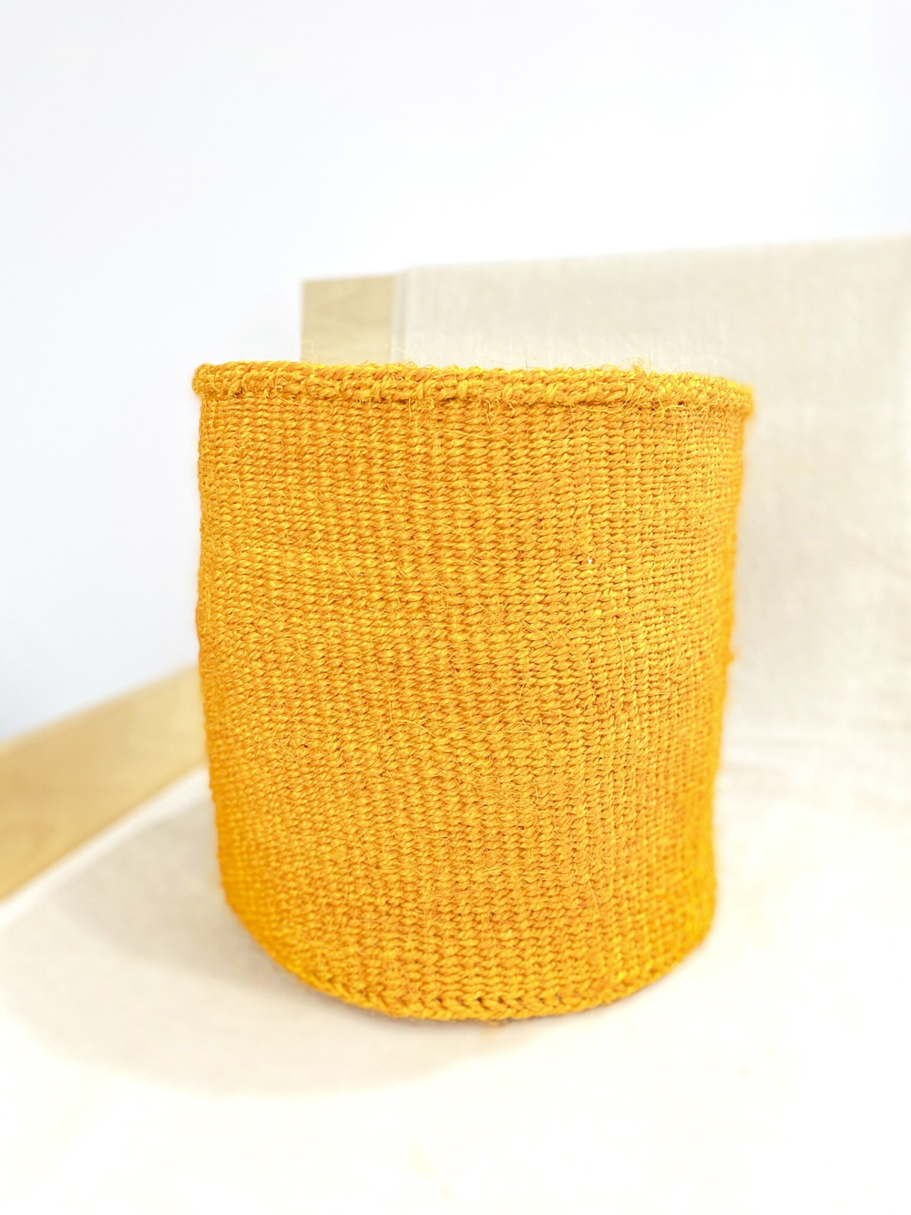 A bold yellow basket handmade in Kenya pictured against a white background