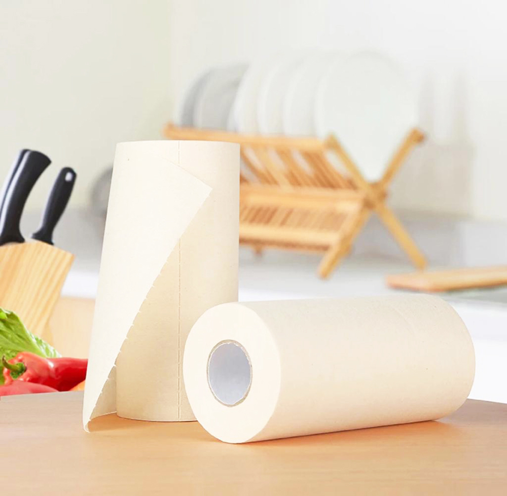 Two rolls of white bamboo paper towel, one standing upright and the other horizontal on a wooden kitchen table