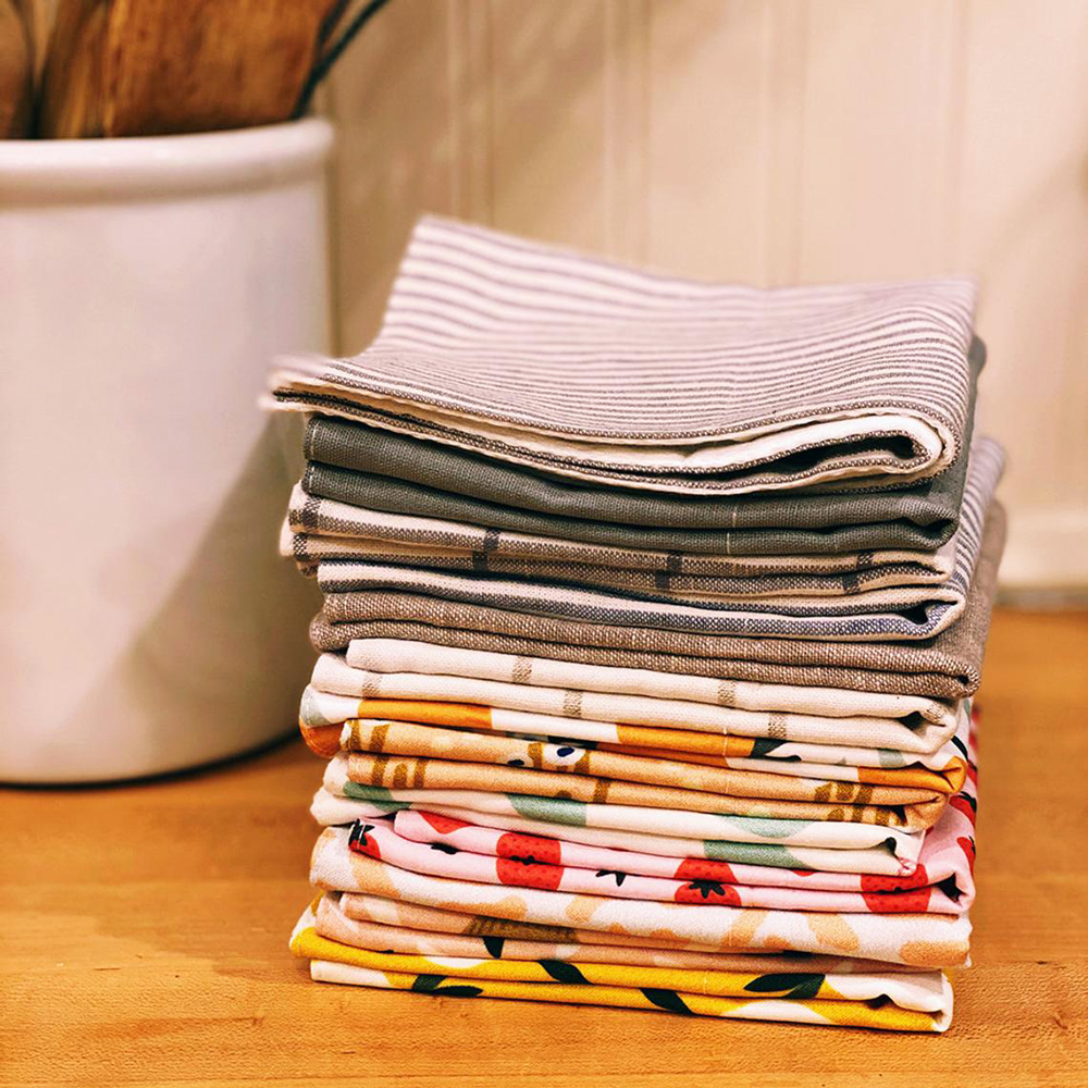 A stack of multi-coloured and patterned cotton paperless towels neatly folded on a kitchen table