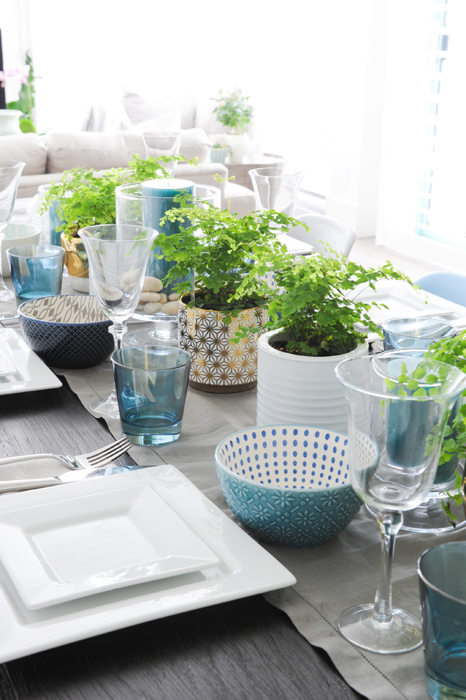 table runner and centrepiece with white square plates, blue glasses and potted greenery