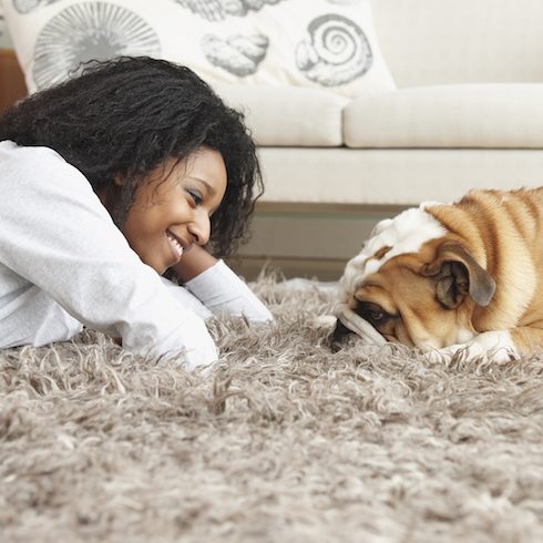 woman laying on beige rug with dog