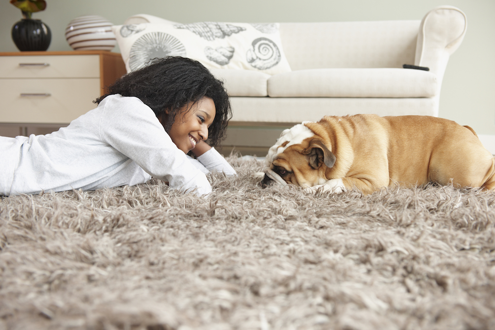 woman laying on beige rug with dog