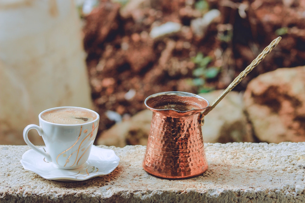 copper cezve and mug with coffee on stone wall
