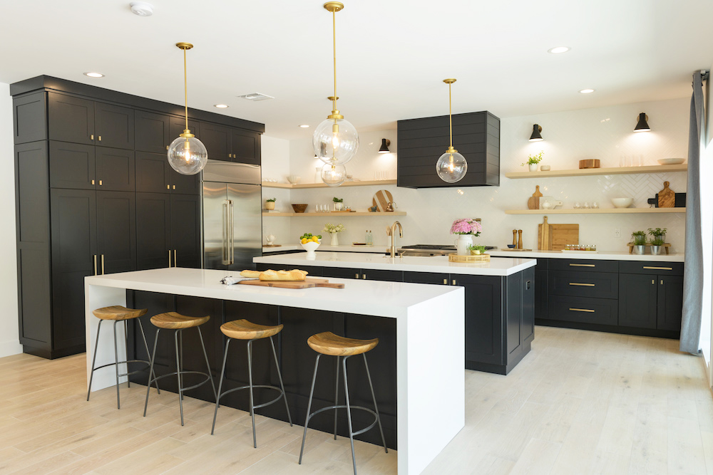 A renovated kitchen with dark cabinetry, dual sister islands and pendant lighting with gold accents