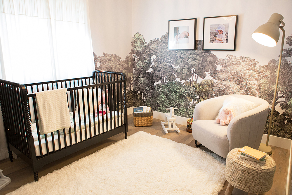 A unisex nursery with brown crib, beige furniture and tree-print wallpaper