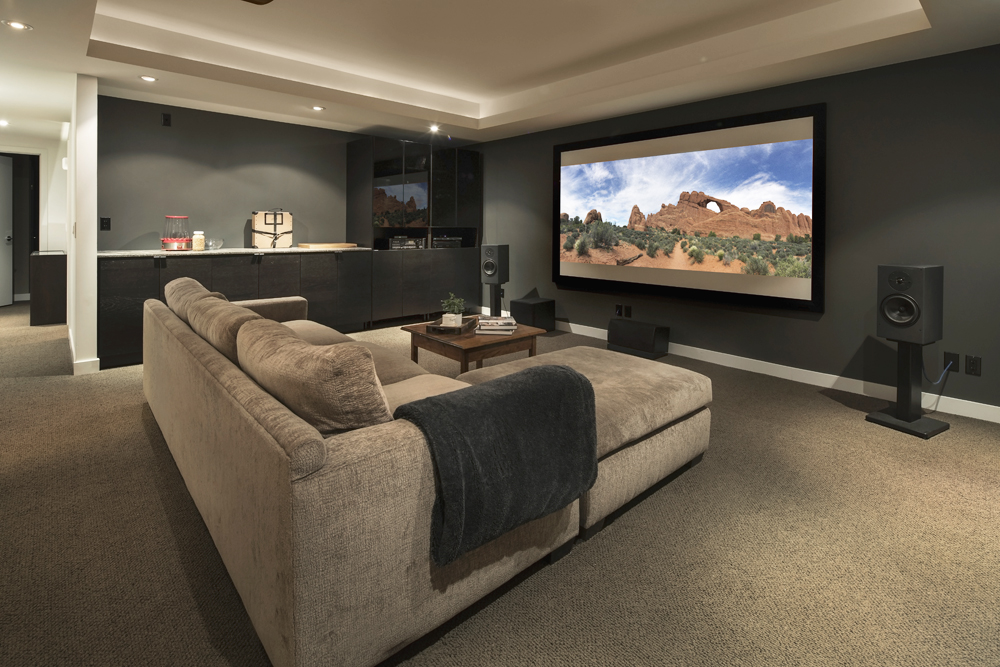 A basement living room decked out like a home movie theatre, complete with large screen and surround sound speakers