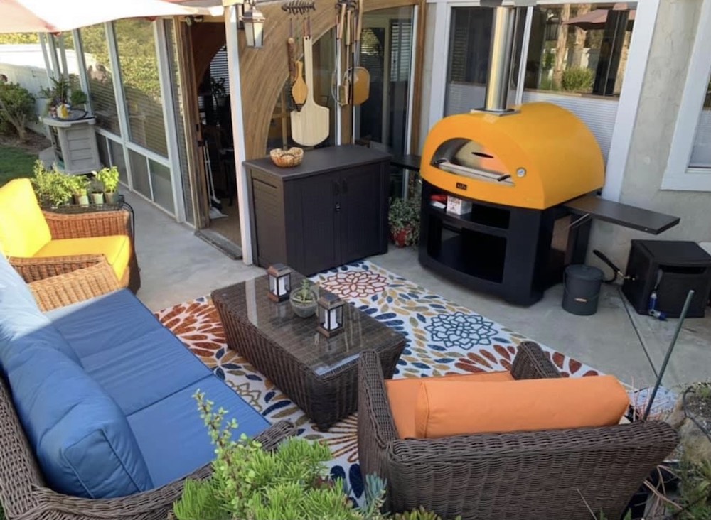 Orange pizza oven in backyard with wicker furniture