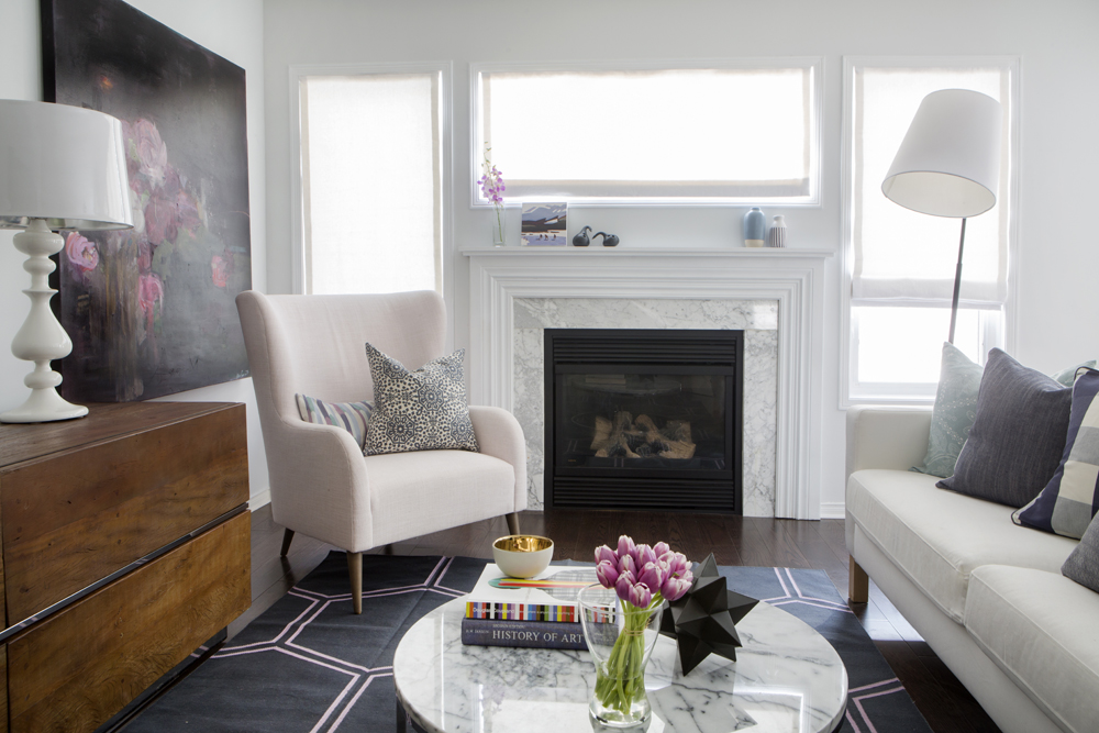white and marble fireplace framed by windows with over-sized armchair in front of it