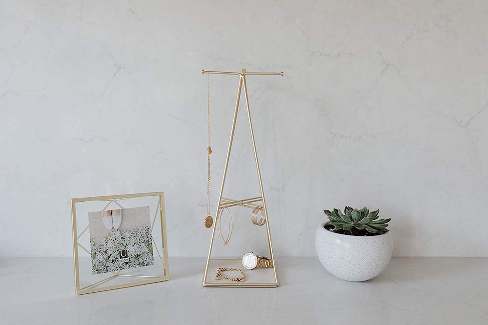 gold jewelry stand, picture frame and potted plant on white counter