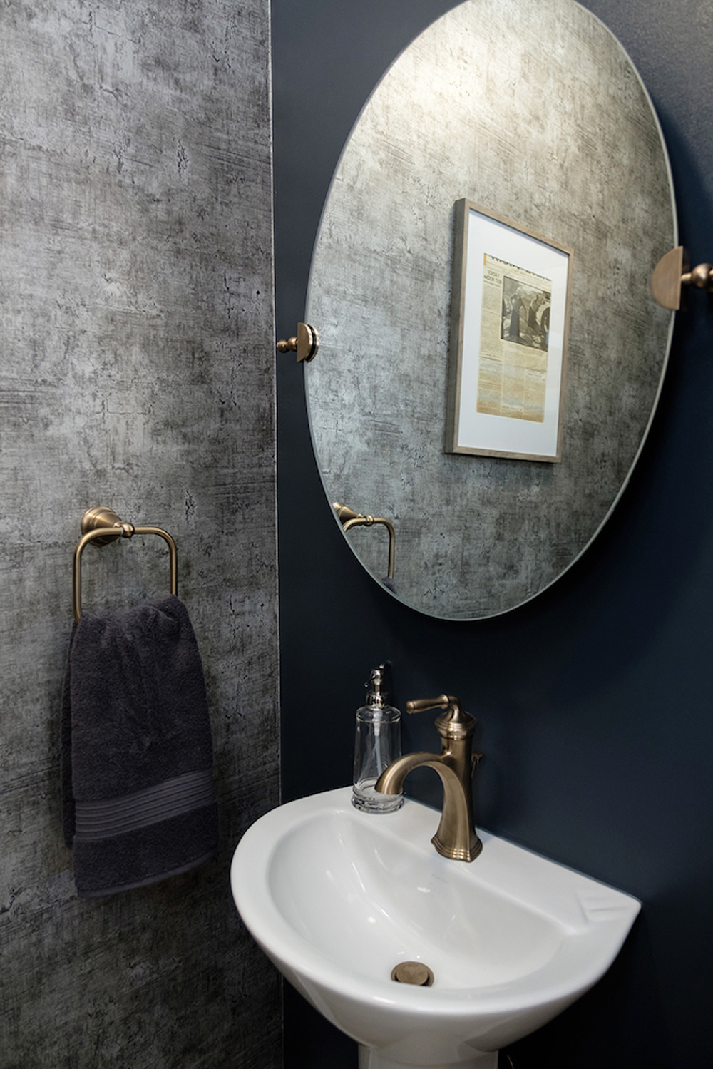 A tiny main floor powder room with aluminum coloured wallpaper and brass fixtures