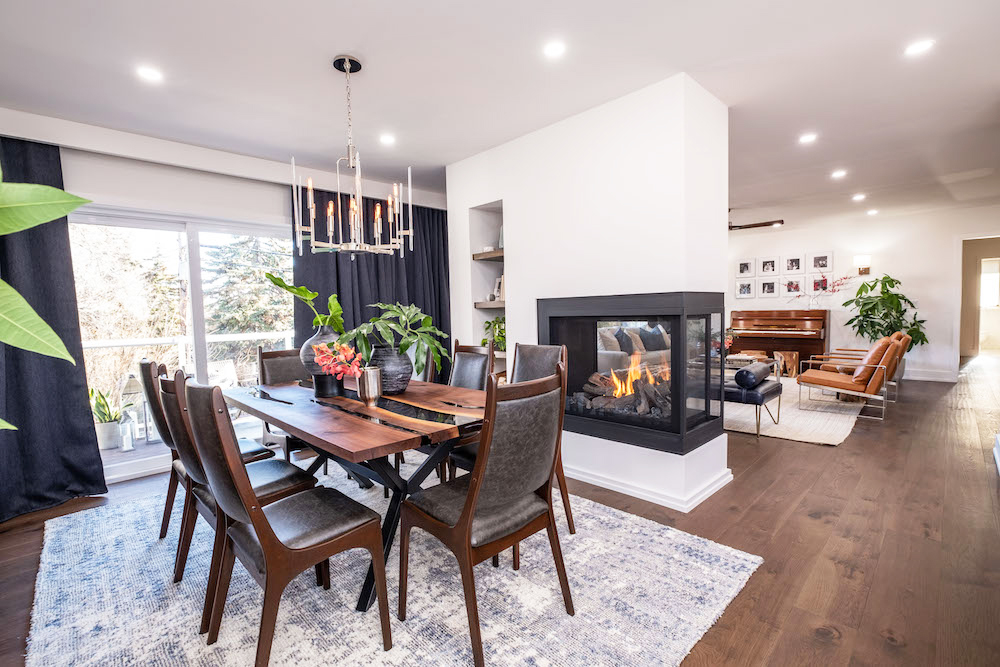 A three-way fireplace separates a kitchen and dining room in this modern renovated bungalow