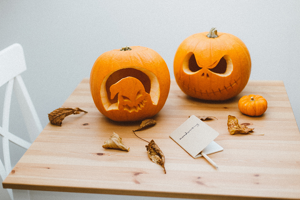Two carved pumpkins sitting on a wood kitchen table