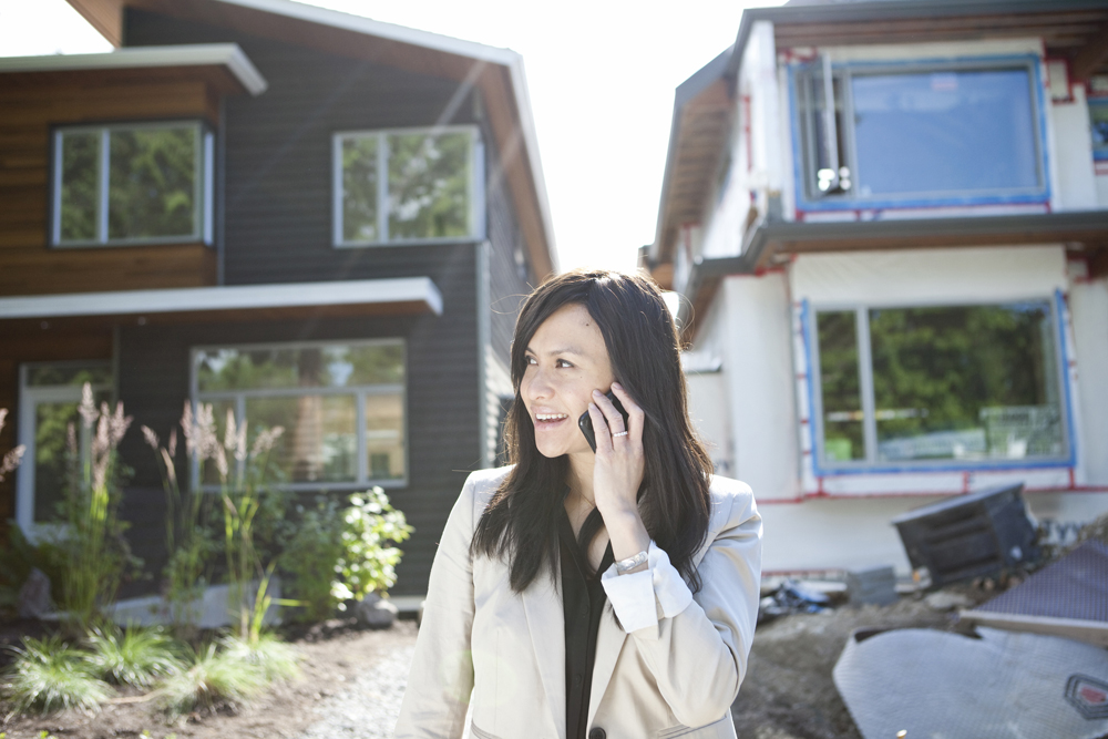 Mixed race real estate agent standing near house talking on cell phone
