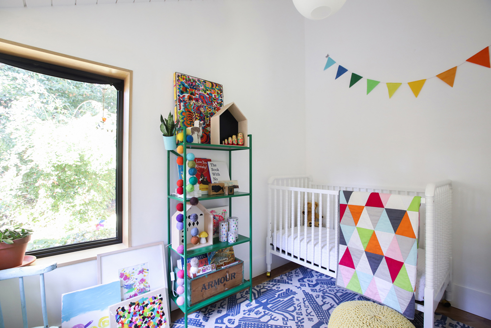 white walled nursery with green shelving unit and colourful triangle quilt over crib