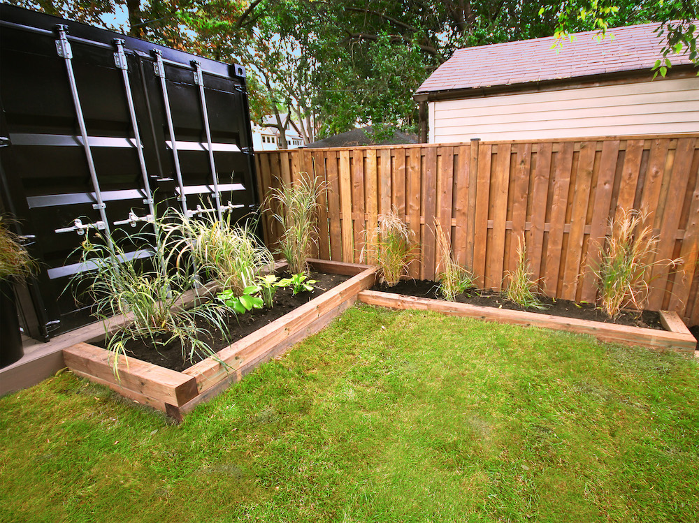 wooden garden beds alongside wooden fence and black shipping container