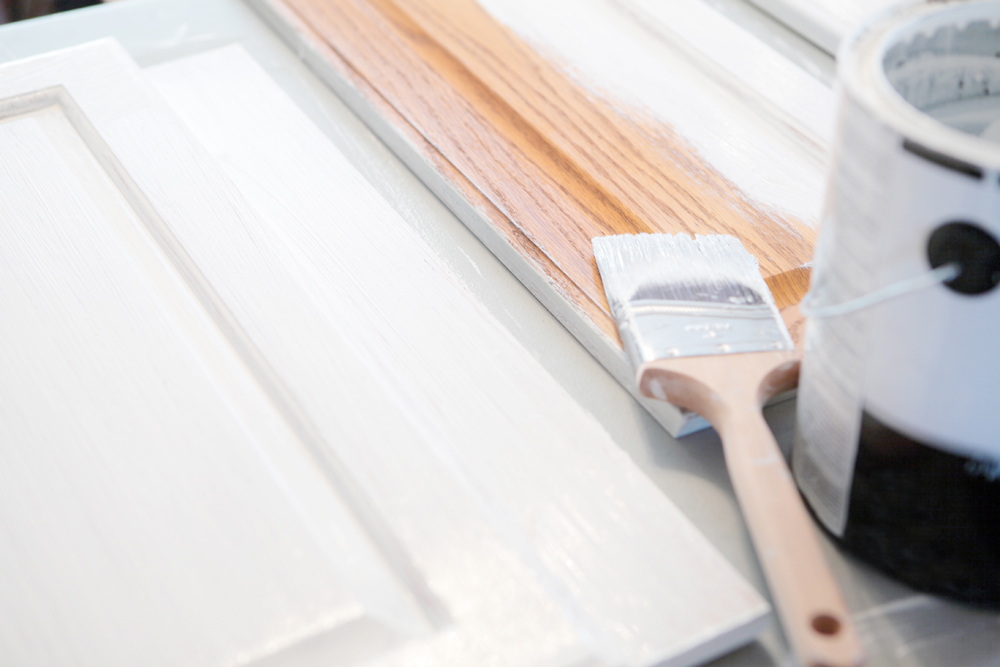 Wooden kitchen cabinets being painted white with a paint brush