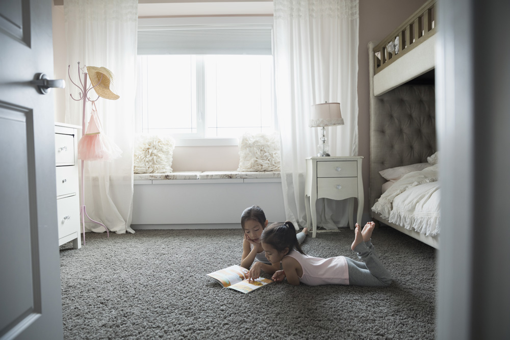 Two little girls reading together on the bedroom carpet