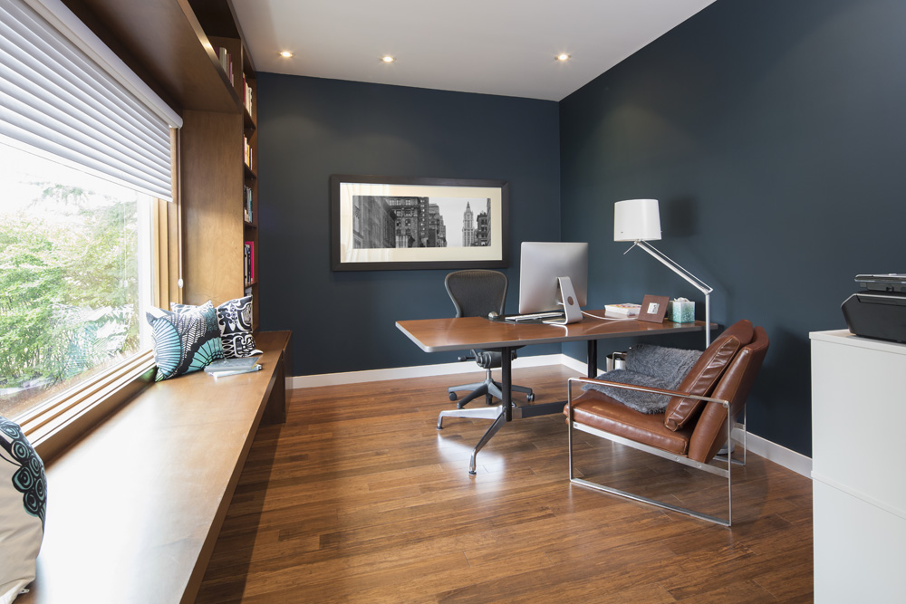 A home office with hardwood floors, grey walls and plenty of light from the window