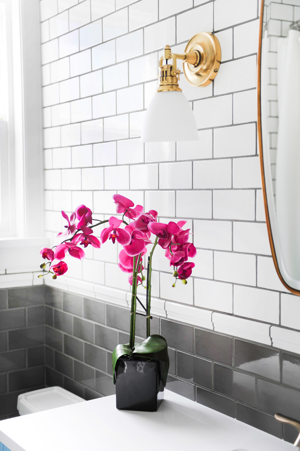 pink orchids in black square vessel in grey and white bathroom