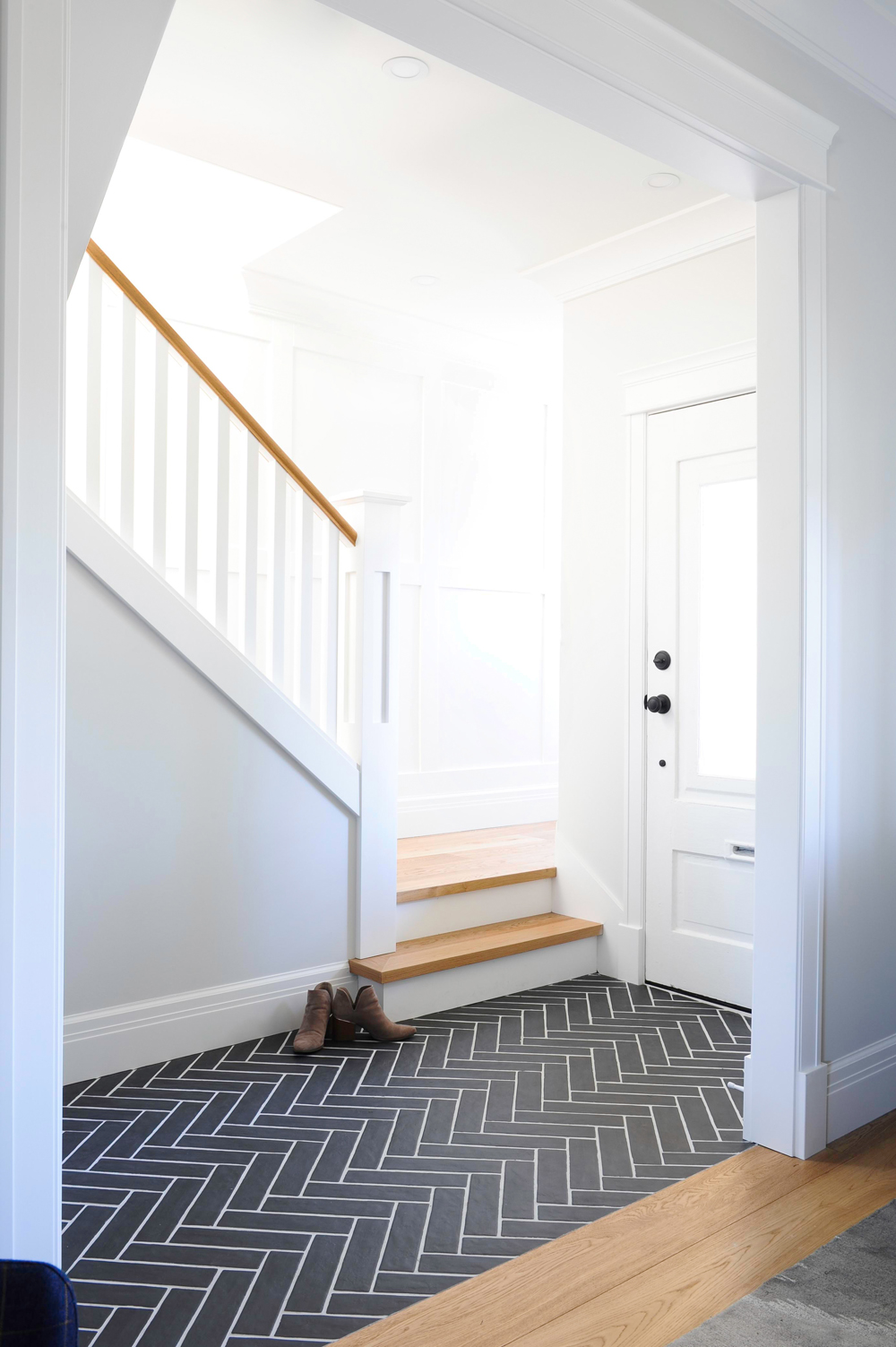 white front hall and staircase with grey tile and white grout herringbone floor