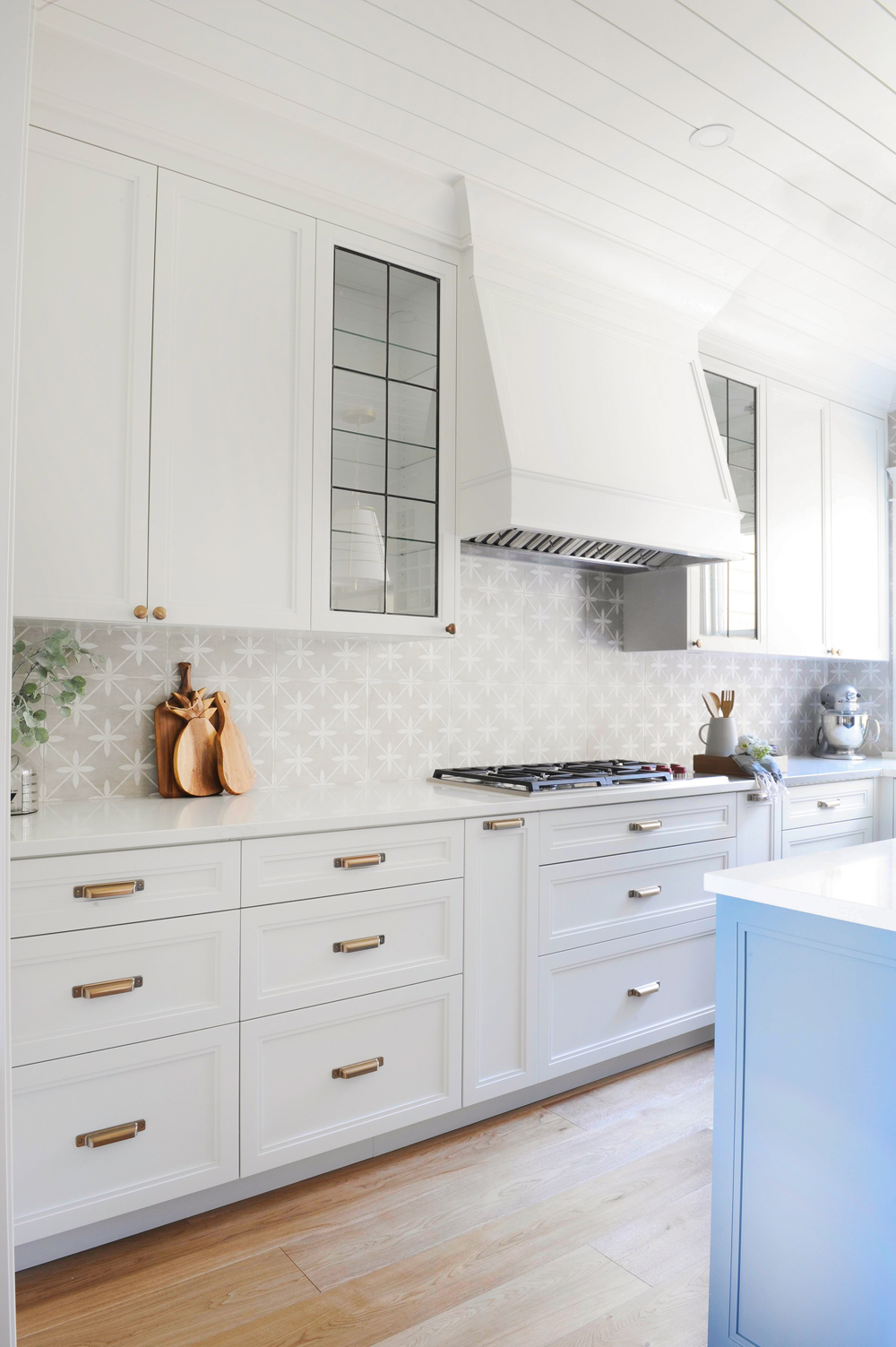 white kitchen with brass pulls and edge of blue island in right foreground