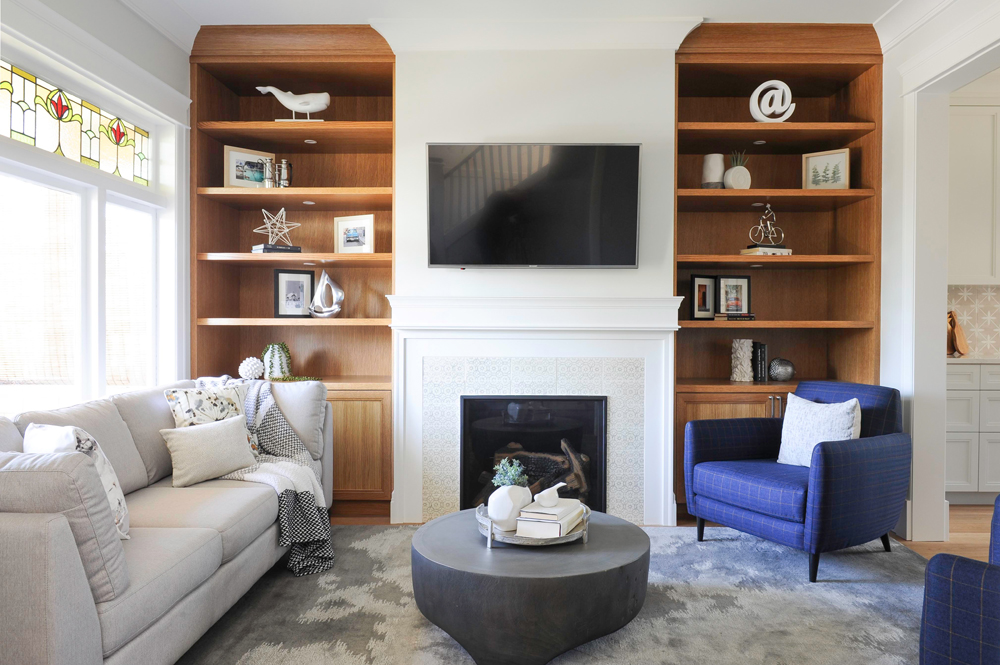 living room white fireplace with TV above, flanking walnut shelves and blue plaid chairs