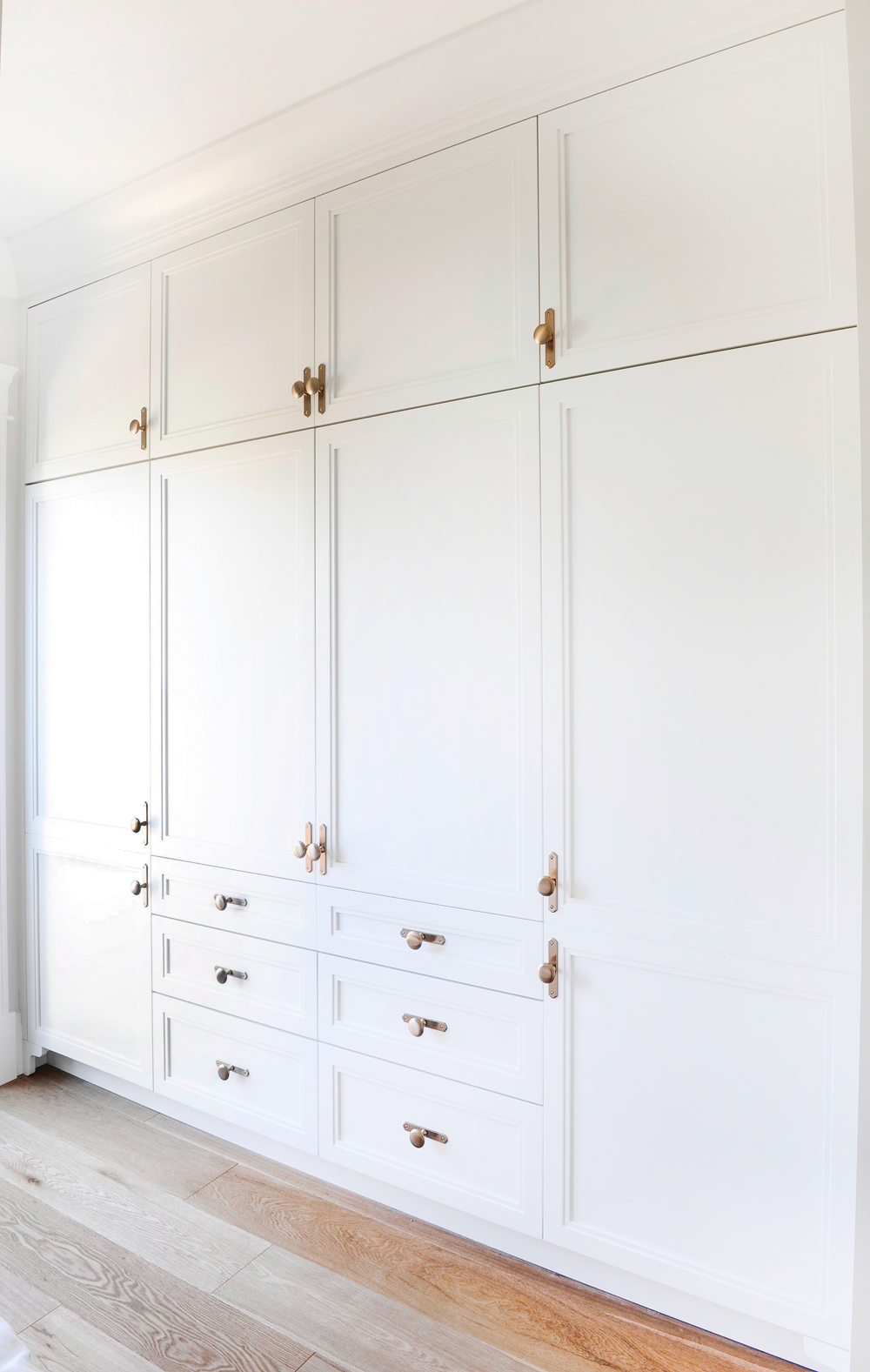 white floor to ceiling drawers and cabinets with brass hardware