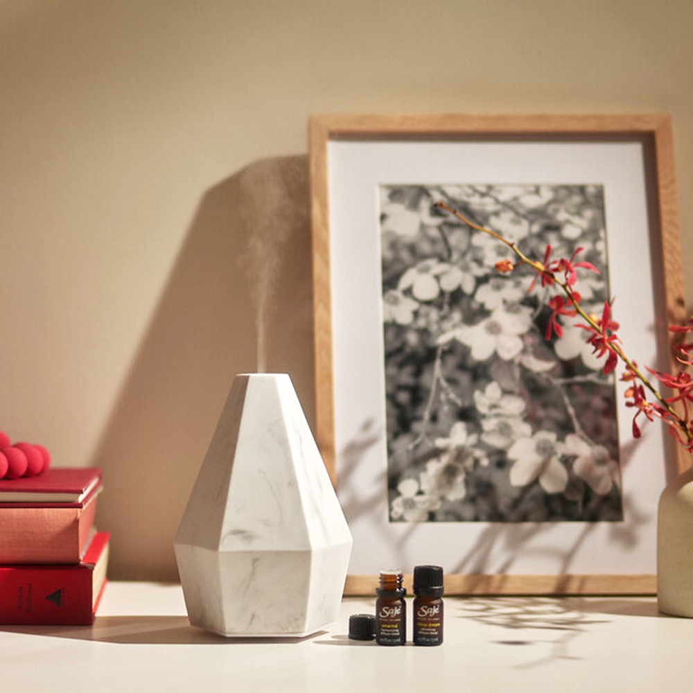 A white marble diffuser with two essential oils next to it on a well-organized decorated desk