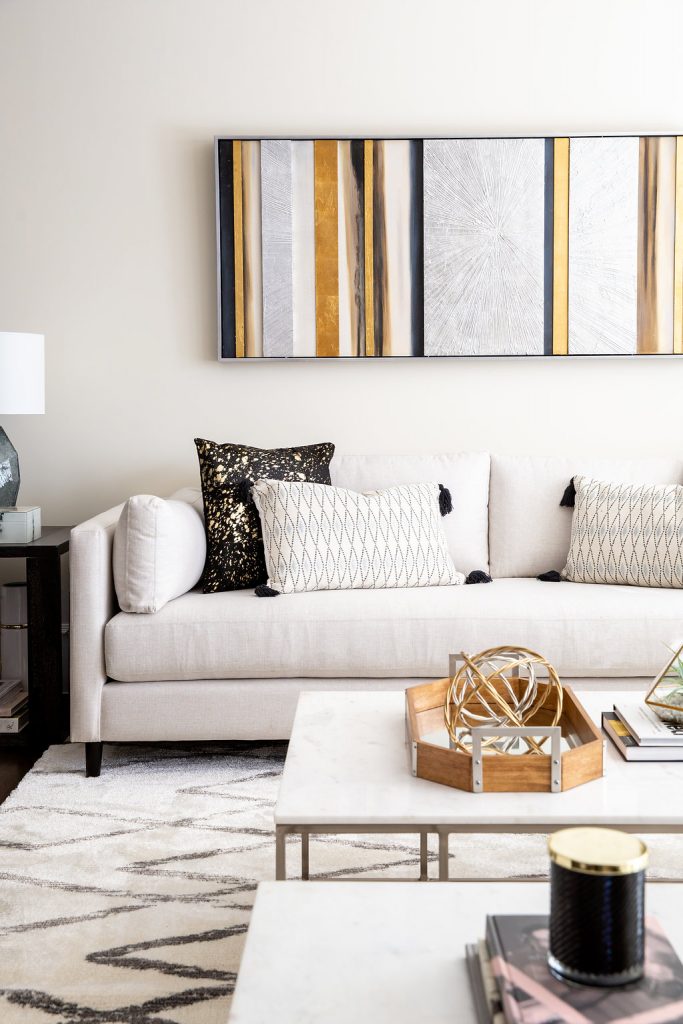 Black, gold and white vertical artwork above cream sofa with cushions