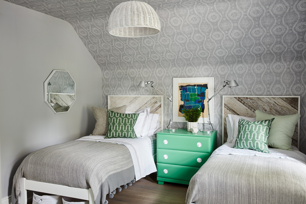 Sloped bedroom ceiling with wallpaper and two single beds with bright mint green nightstand separating them