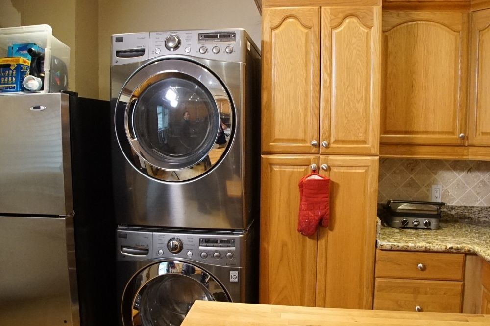 An outdated kitchen with blond cabinetry and a stacked washer/dryer