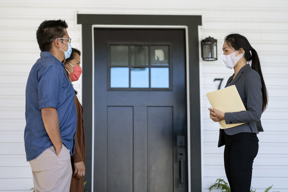 Real Estate agent meeting with clients outside front door, in masks